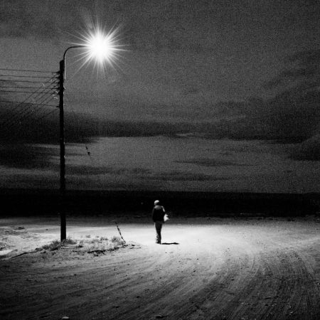Black and white image of a man beneath a lamp post at night